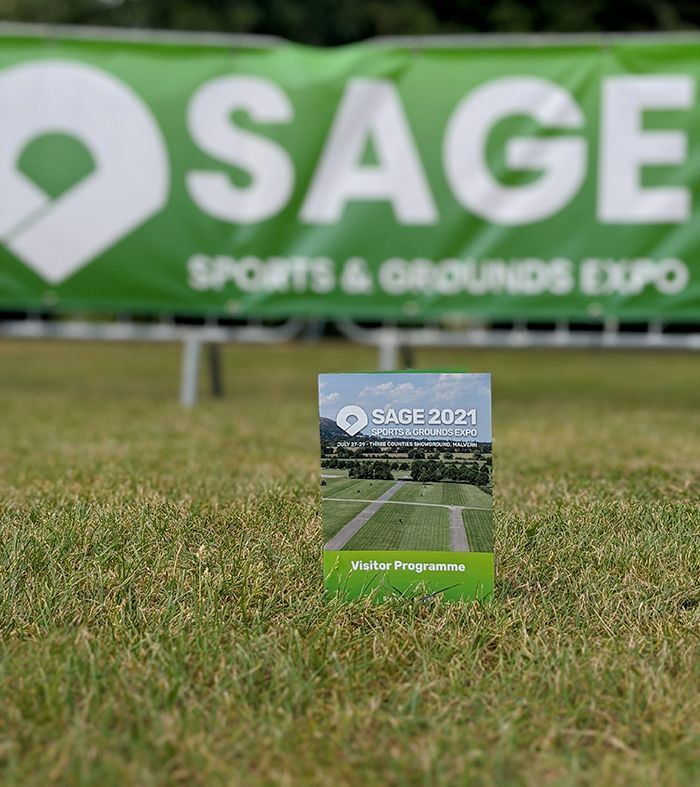 SAGE (Sports & Grounds Expo) brochure, in a field in front of the SAGE banner