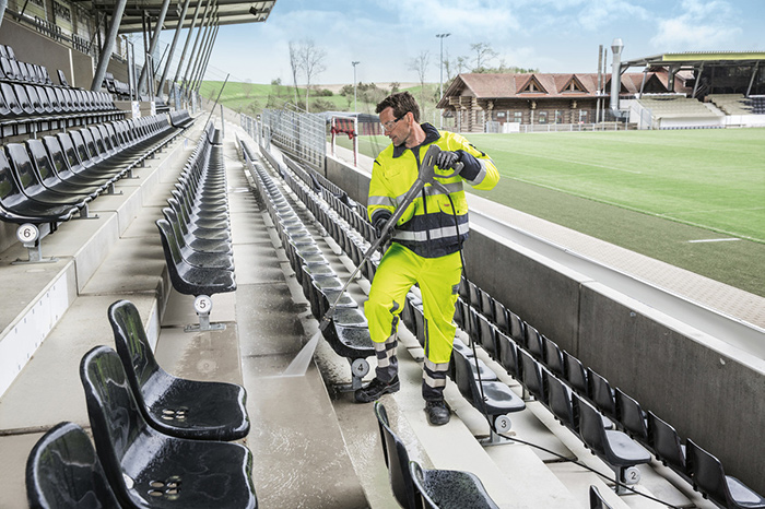 A Kärcher operative power cleaning the floor of a seating area in a football stadium