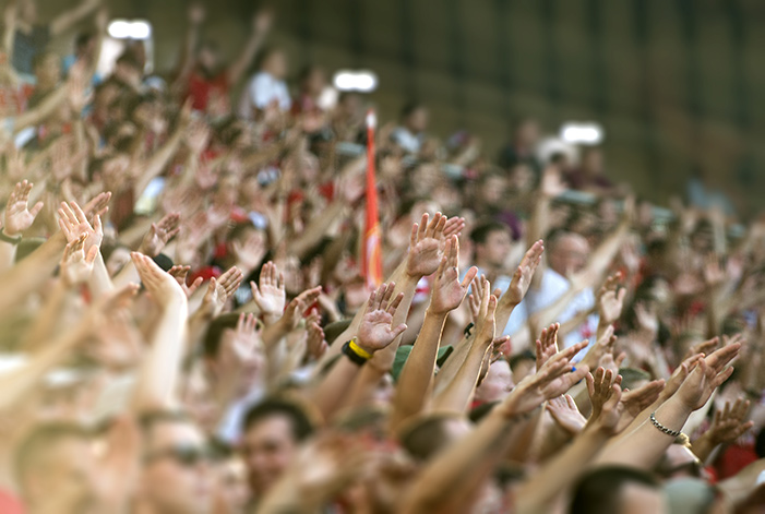 A crowd of spectators at a football match with their hands in the air