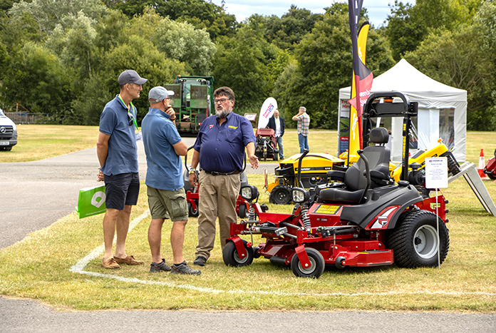 An exhibitor talking to two visitors about turf cutting machinery