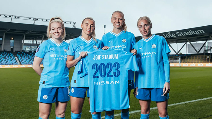 Manchester City Women's team holding a football shirt branded with Joie stadium