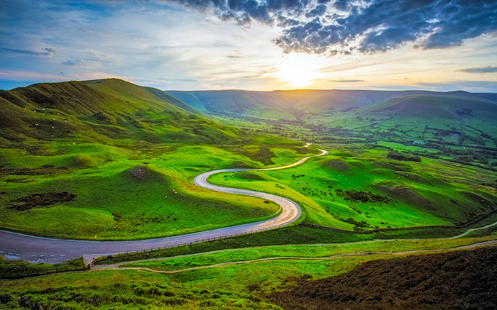 The sun shining on a winding road between green hills