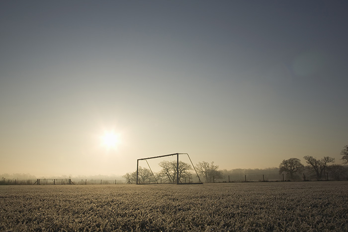 A desolate-looking, frozen sports ground with a lone, frosted goal post