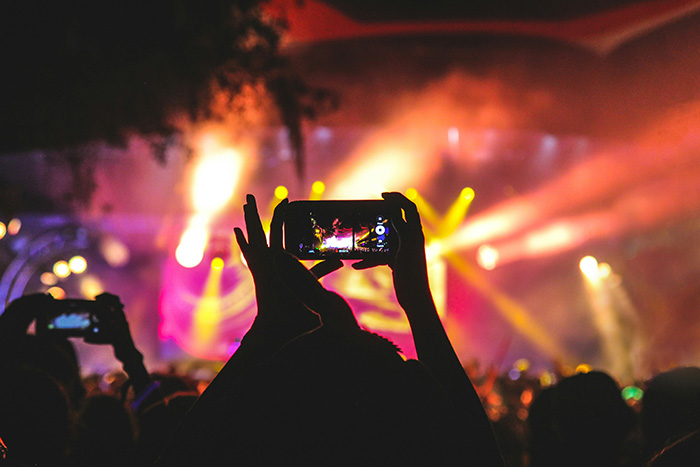 A person using a phone at a concert while watching a music band