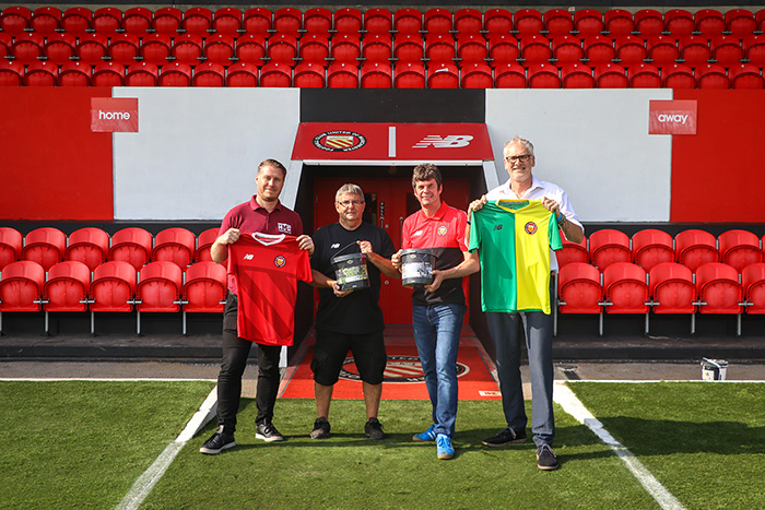 Staff from HMG posing on FC United Of Manchester's ground to celebrate their partnership